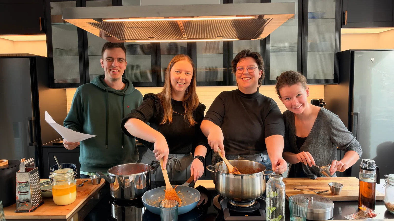 Vier deelnemers lachend achter het fornuis tijdens een workshop